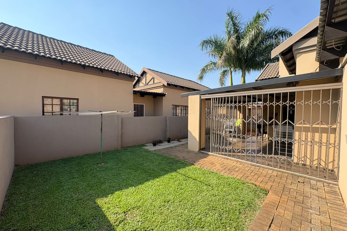 A private rear garden featuring a paved walkway, a well-maintained lawn, and a covered patio area secured with a metal gate.