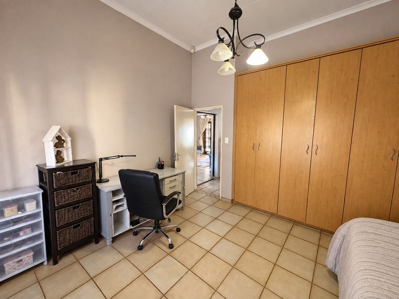 A bedroom featuring built-in wooden cupboards, tiled flooring, and a central light fixture, offering a functional space with direct access to the hallway.