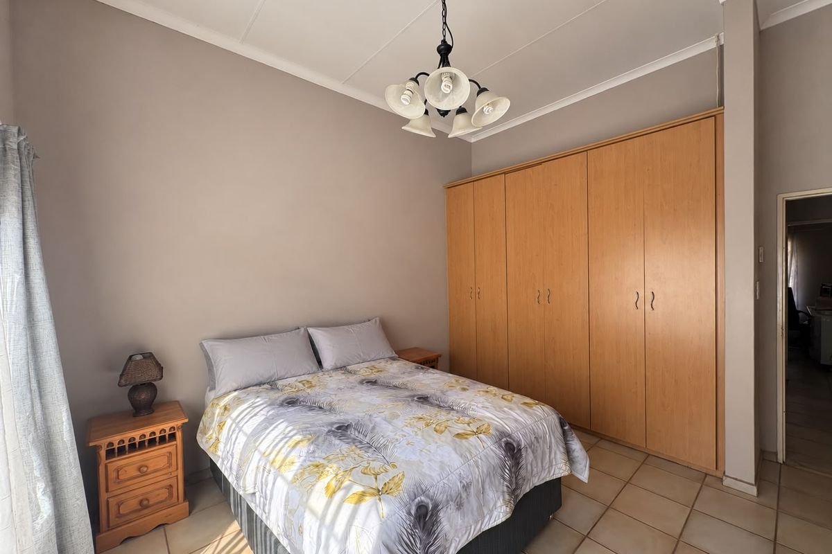 A bedroom featuring built-in wooden cupboards, tiled flooring, and a central ceiling light fixture.