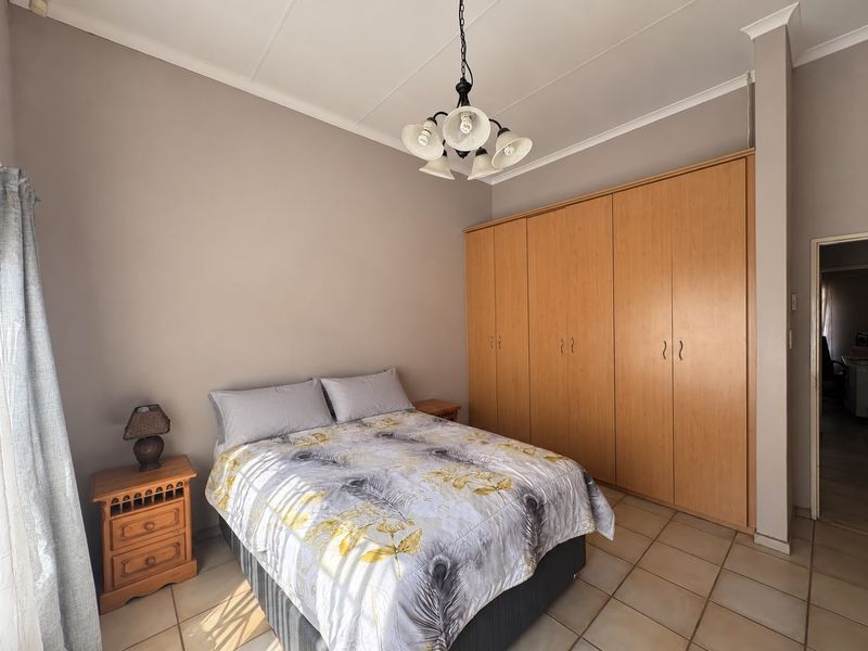 A bedroom featuring built-in wooden cupboards, tiled flooring, and a central ceiling light fixture.