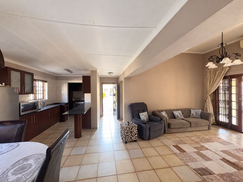 Open-plan living and kitchen area featuring tiled flooring, dark wood cabinetry, and direct access to the exterior through a security-fitted sliding door.