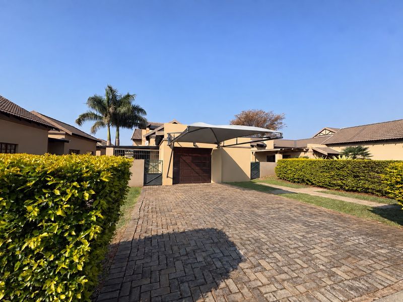 Front exterior view of the townhouse featuring a paved driveway, a shade sail carport, a garage, and well-maintained garden hedges.