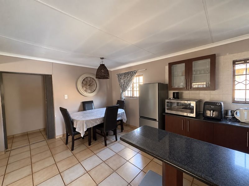 Open-plan kitchen and dining area featuring dark wood cabinetry, granite countertops, tiled flooring, and a functional layout with a breakfast bar.