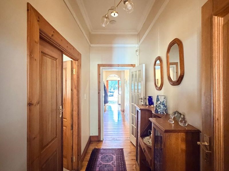 A well-maintained hallway featuring polished timber flooring, classic timber door frames, and decorative ceiling cornicing, leading through to an adjacent living space.