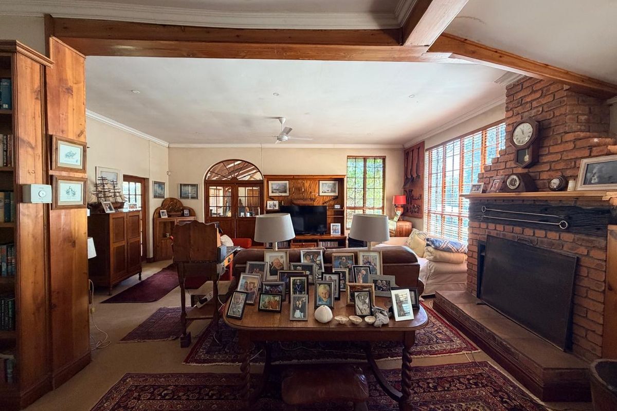 Spacious living room featuring a prominent brick fireplace, exposed timber ceiling beams, and built-in cabinetry, offering a traditional and cozy atmosphere.