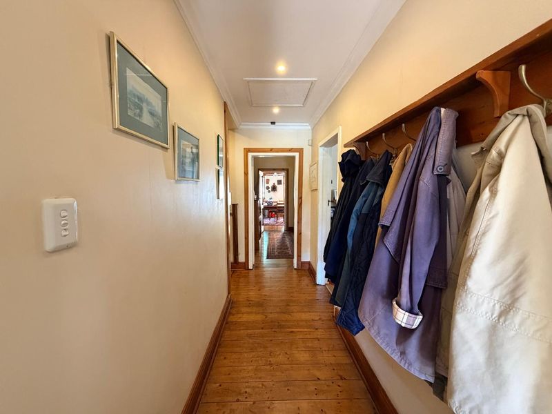 A well-maintained hallway featuring warm timber flooring, recessed ceiling lighting, and a practical wall-mounted coat rack, leading through to the main living areas.