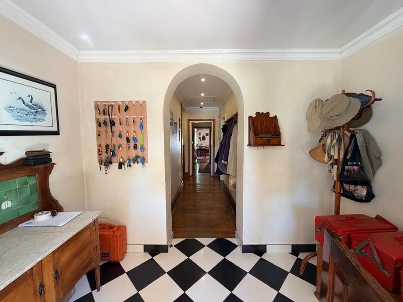 A welcoming entrance hall featuring classic black and white checkered floor tiles, an elegant arched doorway, and a transition into a hardwood floored hallway.