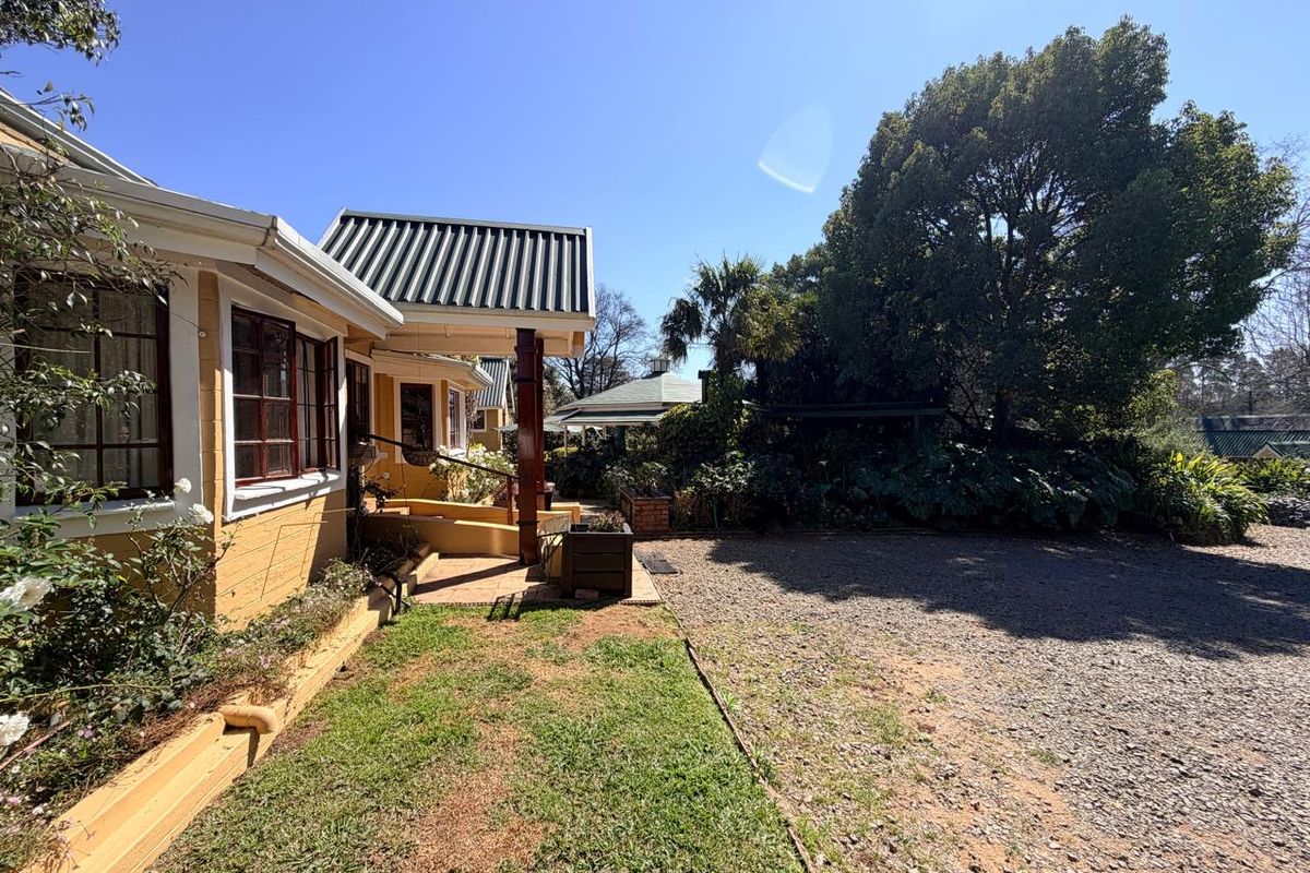 Rear exterior view of the property featuring a covered walkway, gravel driveway, and established garden surroundings.