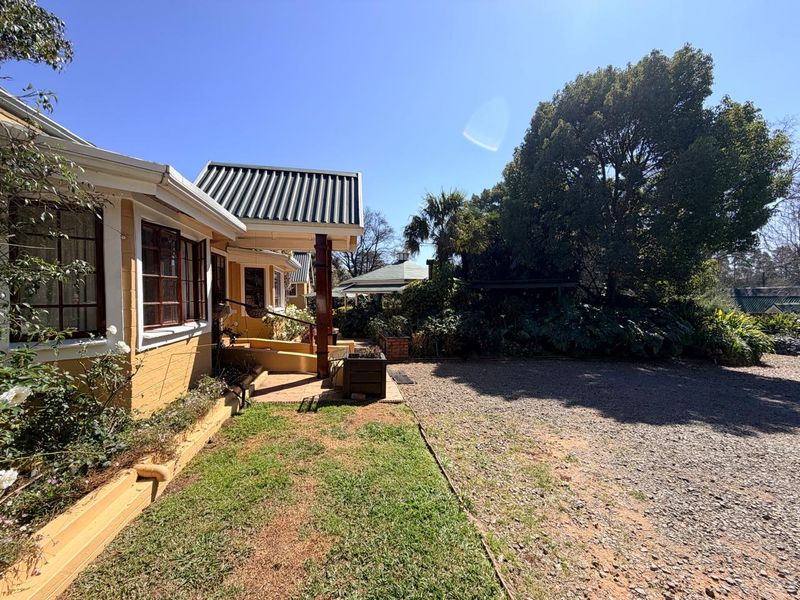 Rear exterior view of the property featuring a covered walkway, gravel driveway, and established garden surroundings.