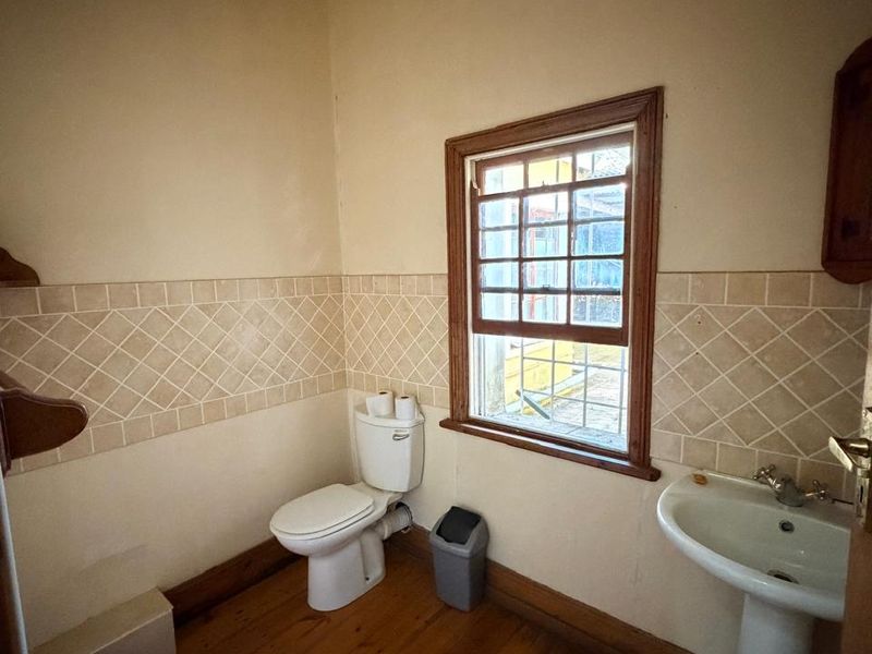 A functional bathroom featuring a pedestal basin, toilet, bidet, and timber flooring with a classic tiled splashback.