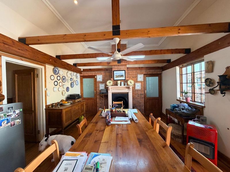 Dining room featuring exposed timber ceiling beams, a brick fireplace, and timber flooring, creating a rustic and character-filled atmosphere.