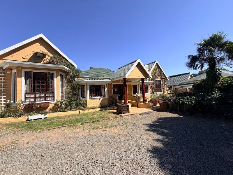 Front elevation of a charming house featuring a pitched metal roof, timber-framed windows, and a covered entrance porch, set on a gravel driveway.