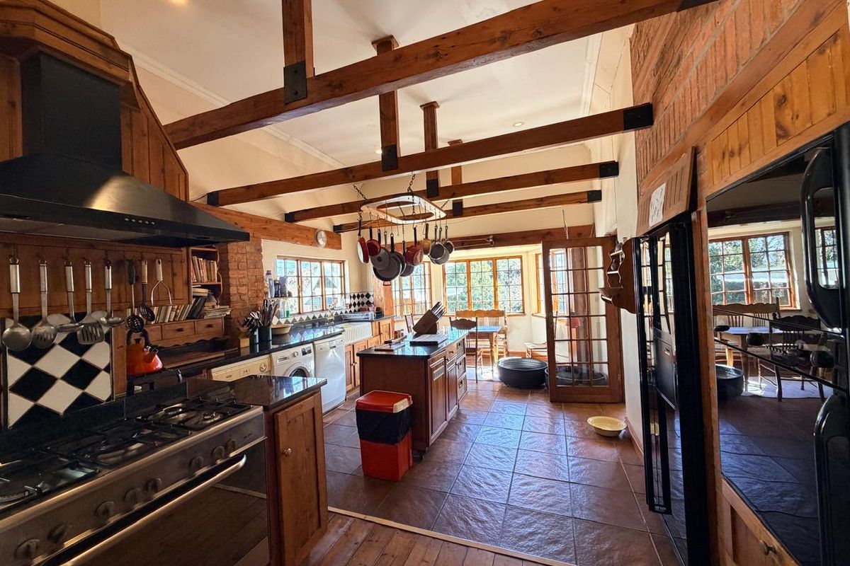 Spacious rustic kitchen featuring exposed timber beams, brick accents, granite countertops, a gas range, and direct access to an adjoining dining area.