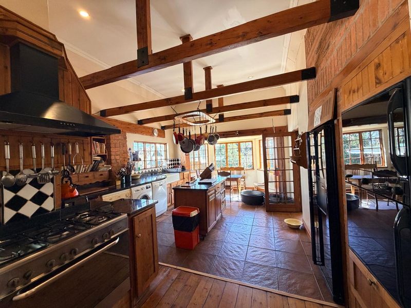 Spacious rustic kitchen featuring exposed timber beams, brick accents, granite countertops, a gas range, and direct access to an adjoining dining area.