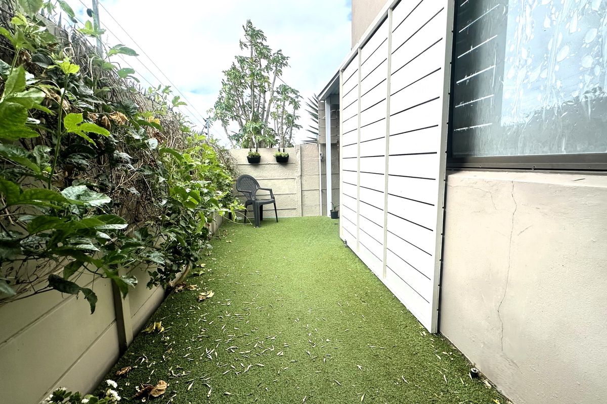 A narrow rear garden area featuring artificial turf, a white privacy screen, and a concrete boundary wall with electric fencing.