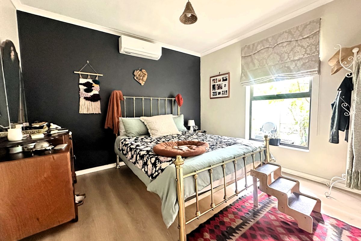 A well-maintained bedroom featuring laminate flooring, a split-system air conditioner, and a large window with a roman blind.