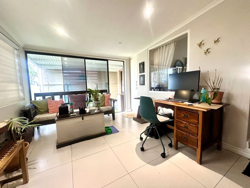A bright living area featuring large sliding glass doors leading to an outdoor space, tiled flooring, and an internal window providing natural light.