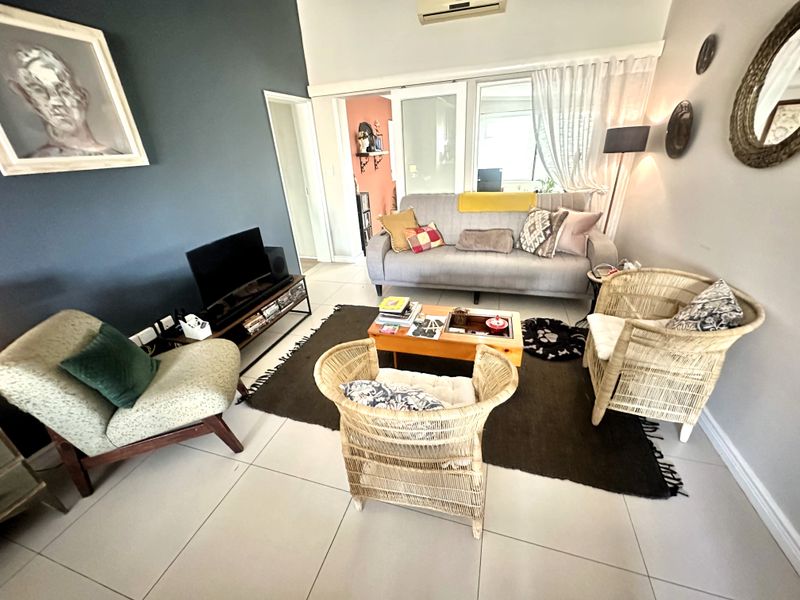 A comfortable living room featuring tiled flooring, a wall-mounted air conditioning unit, and sliding glass doors leading to an adjacent space.