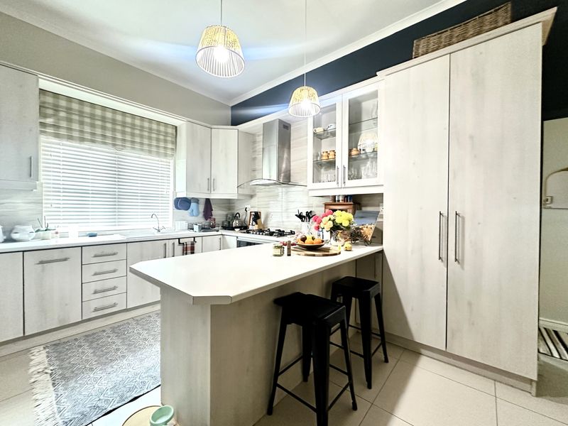 Modern kitchen featuring light wood-grain cabinetry, a central island with breakfast bar, gas hob, extractor fan, and tiled flooring with ample storage space.