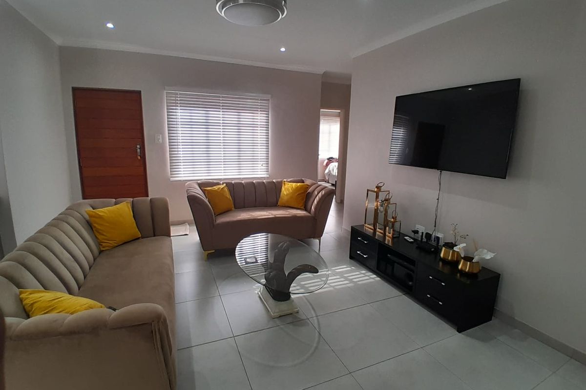 A well-maintained living room featuring neutral tiled flooring, recessed downlighting, and venetian blinds, creating a bright and comfortable living space.