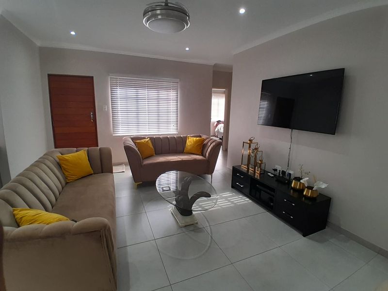 A well-maintained living room featuring neutral tiled flooring, recessed downlighting, and venetian blinds, creating a bright and comfortable living space.