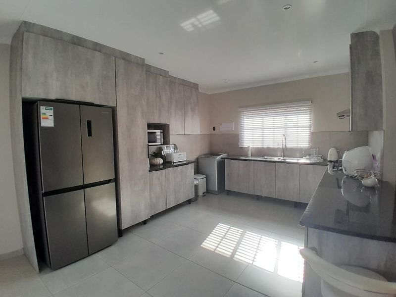 Modern kitchen featuring grey wood-look cabinetry, dark stone countertops, tiled flooring, and integrated storage space with ample natural light.
