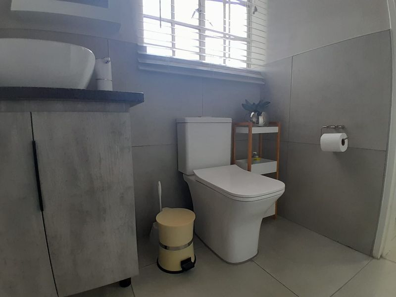 A modern bathroom featuring a vessel sink on a vanity cabinet, a white toilet, and neutral wall tiles with natural light from a window.