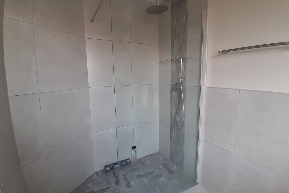 A modern walk-in shower featuring large format wall tiles, a mosaic tiled floor, glass screen, and dual shower heads.