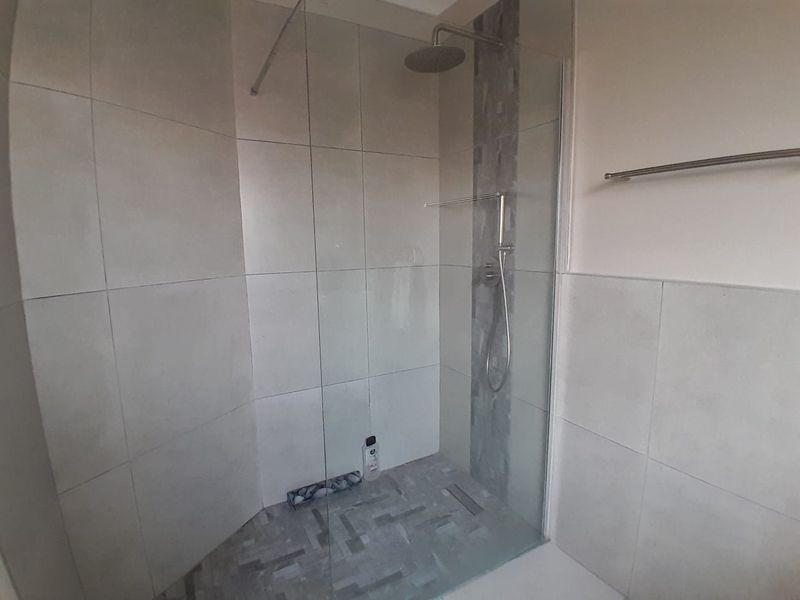 A modern walk-in shower featuring large format wall tiles, a mosaic tiled floor, glass screen, and dual shower heads.