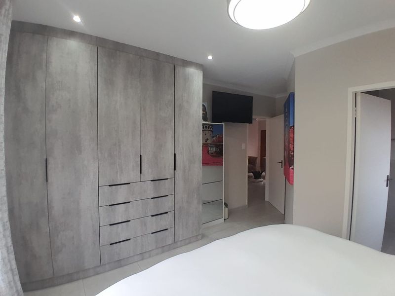 A well-maintained bedroom featuring modern grey built-in wardrobes with integrated drawers and recessed ceiling lighting.