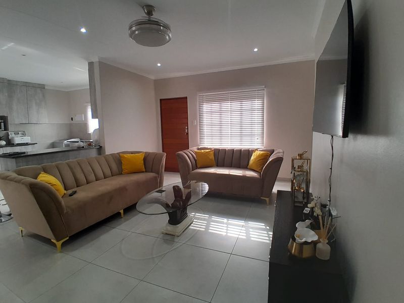 A bright open-plan living area featuring modern tiled flooring, recessed lighting, and a seamless transition into the adjacent kitchen space.