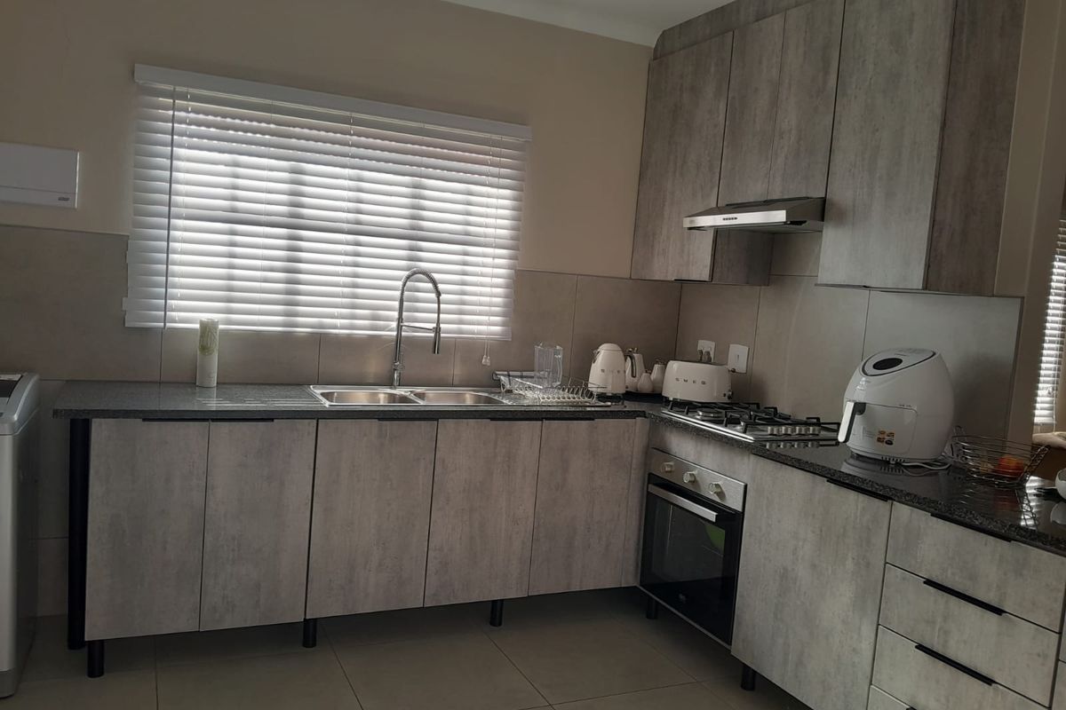 Modern kitchen featuring grey wood-look cabinetry, granite countertops, built-in gas hob, oven, and extractor fan with a tiled backsplash and venetian blinds.