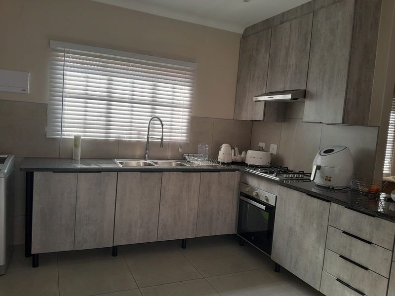 Modern kitchen featuring grey wood-look cabinetry, granite countertops, built-in gas hob, oven, and extractor fan with a tiled backsplash and venetian blinds.