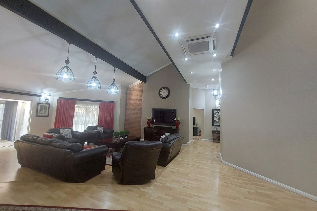 Spacious living room featuring high vaulted ceilings with exposed beams, a brick feature wall, and integrated cassette air conditioning.