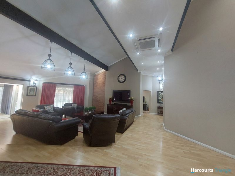 Spacious living room featuring high vaulted ceilings with exposed beams, a brick feature wall, and integrated cassette air conditioning.