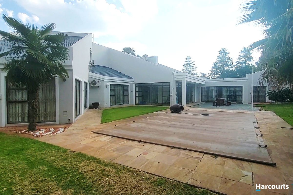 Rear exterior view featuring a swimming pool with cover, paved patio area, and landscaped garden with access via sliding glass doors.