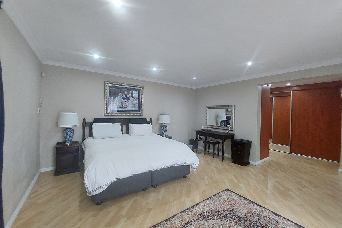 Spacious bedroom featuring light wood herringbone flooring, recessed downlighting, and integrated built-in cupboards with sliding doors.