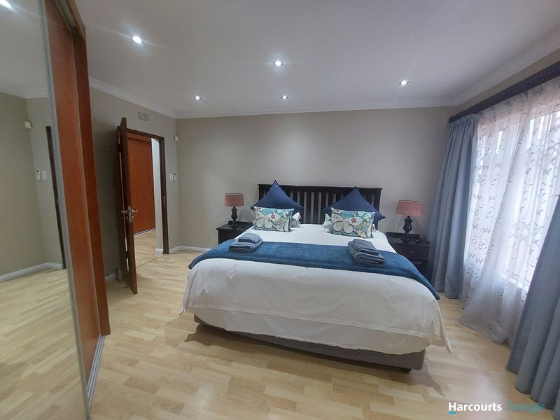 A well-maintained bedroom featuring laminate flooring, recessed downlighting, and built-in cupboards with sliding mirror doors.