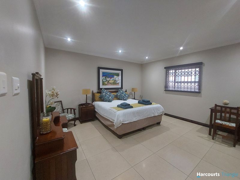 A spacious bedroom featuring neutral tiled flooring, recessed downlighting, and a window fitted with security bars and venetian blinds.