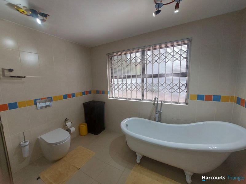 A well-maintained bathroom featuring a classic freestanding bathtub, wall-mounted toilet with concealed cistern, and decorative tiled wall accents.