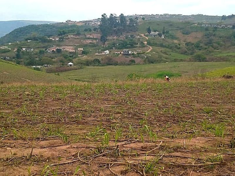 A wide-angle view of open agricultural farmland with rolling hills and distant rural settlement in the background.