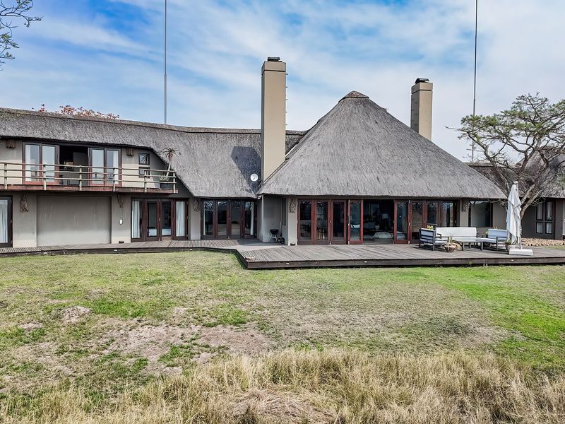 Rear view of a lodge featuring a traditional thatched roof, extensive timber decking, and multiple glass sliding doors opening onto the garden.