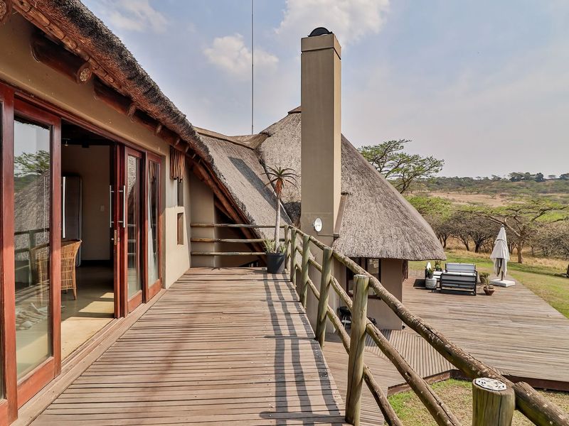Spacious elevated timber deck featuring a thatched roof, timber railings, and a masonry chimney, offering expansive views of the surrounding natural landscape.