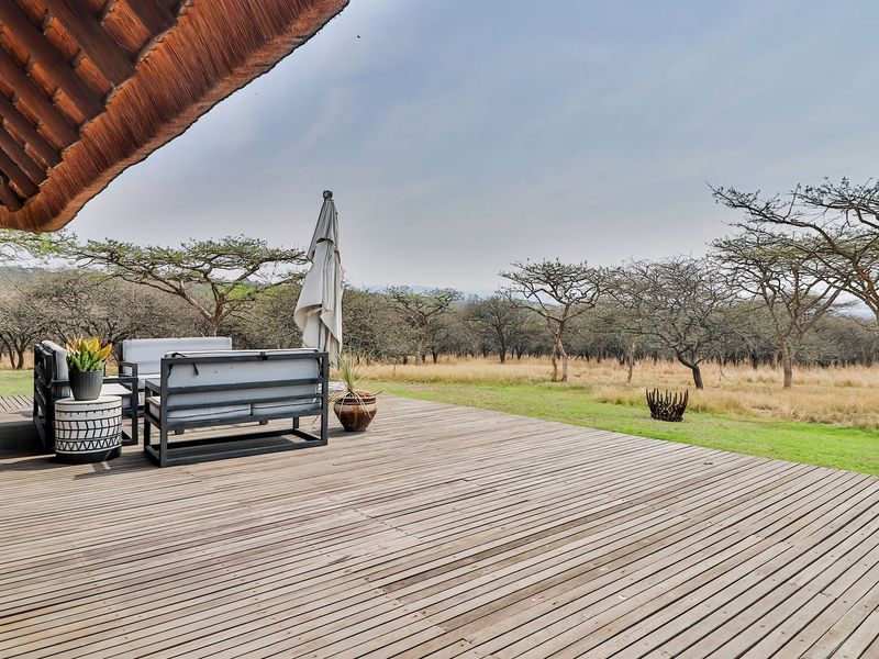Spacious timber deck patio featuring a thatched roof overhang, providing seamless indoor-outdoor flow with expansive views of the surrounding natural landscape.