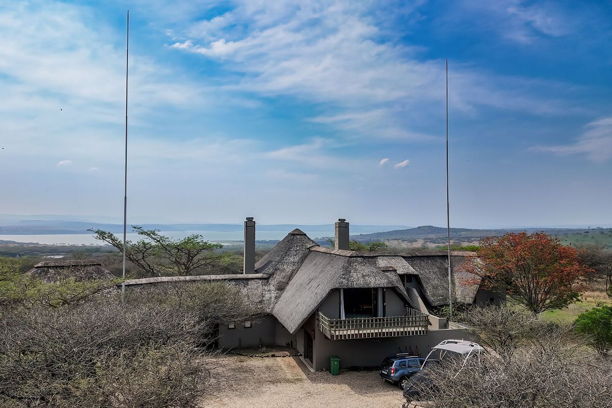 Aerial view of a lodge property featuring a traditional thatched roof, multiple chimneys, and a balcony, set within a scenic landscape.