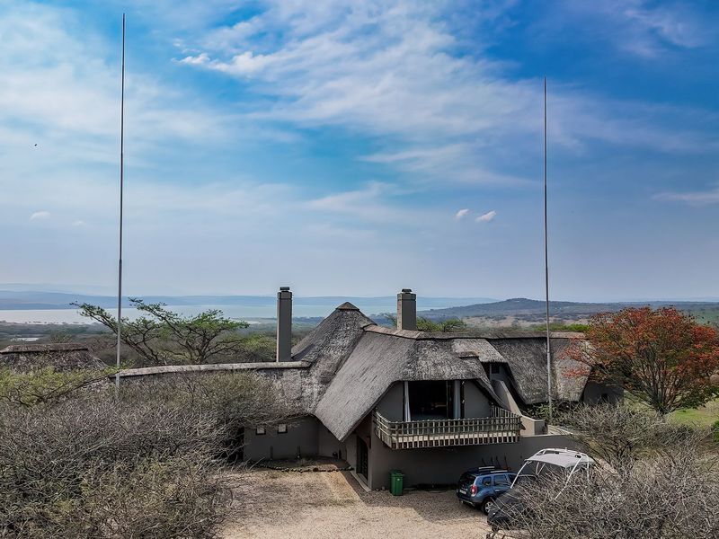 Aerial view of a lodge property featuring a traditional thatched roof, multiple chimneys, and a balcony, set within a scenic landscape.