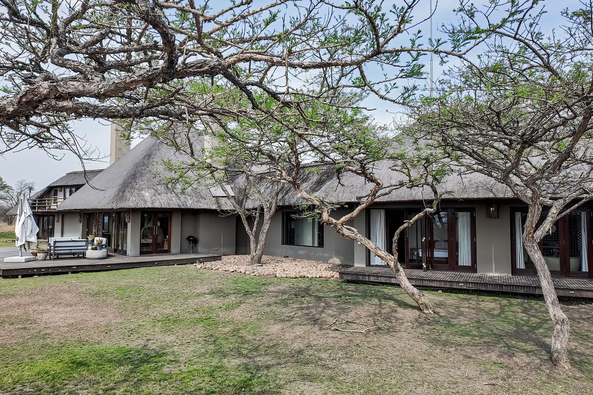 Rear view of a lodge featuring a traditional thatch roof, extensive timber decking, and large sliding glass doors opening onto the garden.