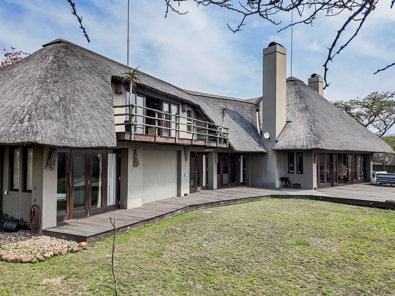 Rear view of a lodge featuring a traditional thatch roof, extensive timber decking, and multiple sliding glass doors leading to the garden.