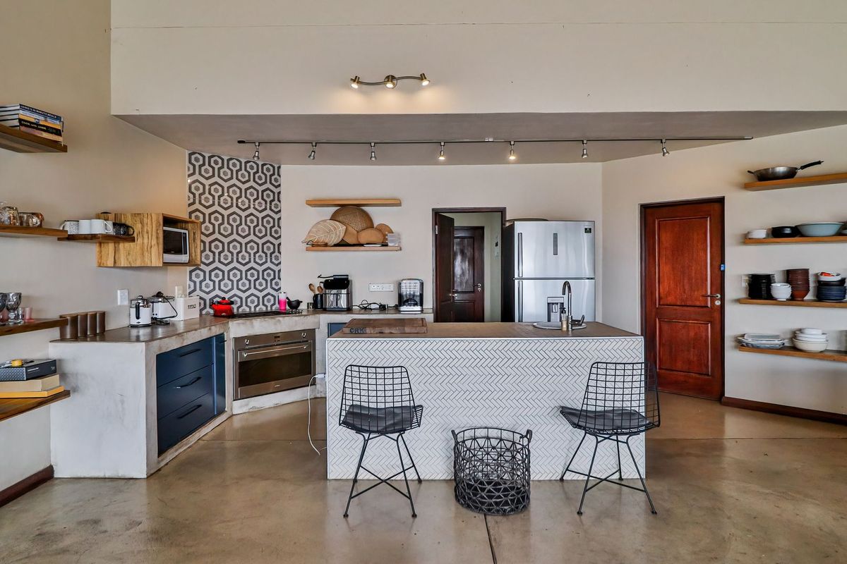 A modern kitchen featuring a central island with a tiled base, built-in oven, sleek cabinetry, and open shelving, set against a neutral backdrop.