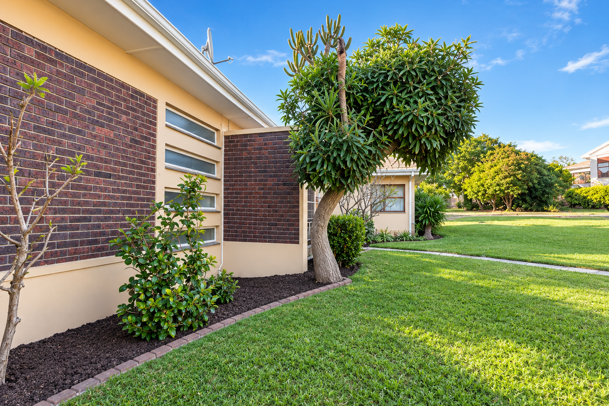 A well-maintained rear exterior view featuring a brick facade, horizontal windows, and a neatly landscaped garden with established trees and lawn.